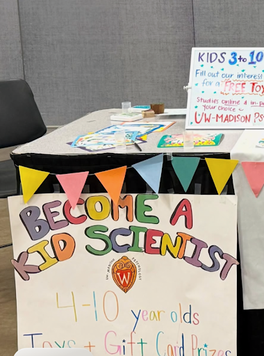 Social and Moral Learning Lab outreach table at the Dane County Fair, featuring a colorful ‘Become a Kid Scientist’ sign, research flyers, and information about participating in studies.