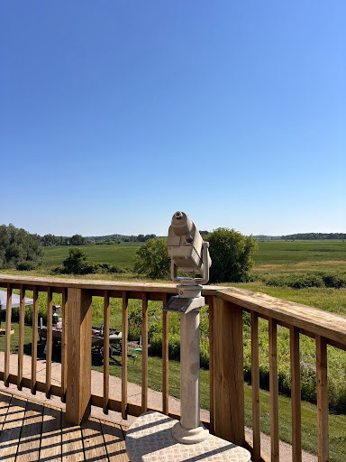 Scenic view from the Lussier Family Heritage Center's observation deck, overlooking green fields and trees under a clear blue sky, with a mounted viewing telescope in the foreground.