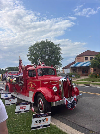 A vintage red fire truck parked along the street at Monona's Community Festival, with other vehicles and festival activities visible in the background.